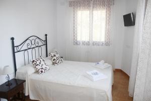 um quarto com uma cama com lençóis brancos e almofadas em Pensión Algarrobeña em Algarrobo