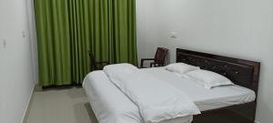 a bedroom with a bed with green curtains and two chairs at RADHA BNB ( HOMESTAY ) in Dharamshala