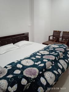 a bed with a blue and white blanket with two chairs at RADHA BNB ( HOMESTAY ) in Dharamshala
