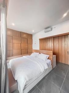 a bedroom with a large white bed with wooden walls at Astakaia Cottage in Ciwidey