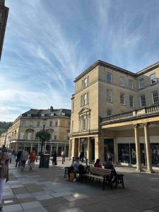 a group of people sitting on benches in front of buildings at Haus of Sulis, City Centre Apartment with Lift Access in Bath