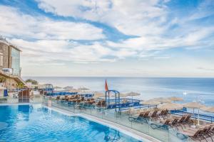 una piscina con sillas y sombrillas y el océano en Club Cala Blanca en Taurito