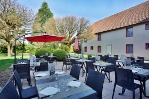 a restaurant with tables and chairs and a red umbrella at Mercure Hexagone Luxeuil in Luxeuil-les-Bains