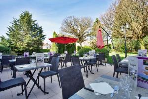 eine Terrasse mit Tischen, Stühlen und einem roten Regenschirm in der Unterkunft Mercure Hexagone Luxeuil in Luxeuil-les-Bains