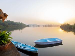 dwie łodzie siedzące na wodzie o zachodzie słońca w obiekcie Mercure Goa Devaaya Resort w mieście Stare Goa