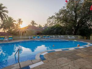 a large blue swimming pool with blue chairs and trees at Mercure Goa Devaaya Resort in Old Goa