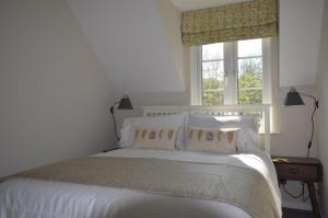 a white bed with white pillows and a window at Elouera, 21 Isis Lake in South Cerney