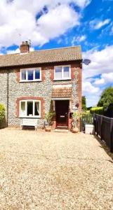 a brick house with a red door on a gravel driveway at Charming North Norfolk flint cottage in Baconsthorpe