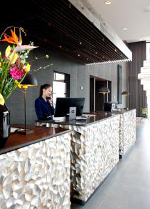 a woman is talking on a phone at a reception desk at Van der Valk Hotel Leeuwarden in Leeuwarden