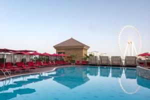 a swimming pool with chairs and a ferris wheel at Amwaj Rotana, Jumeirah Beach - Dubai in Dubai