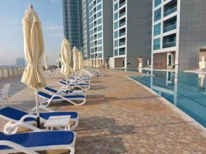 a row of lounge chairs and umbrellas next to a pool at Cozy 1BH Apt next to the sea! in Ajman 