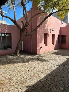 un edificio rosa con un árbol delante de él en Hostel El Puesto en San Antonio de Areco