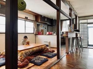 una mujer sentada en una mesa de madera en una cocina en 北アルプス麓のゲストハウス林屋 203 en Ō-shinden