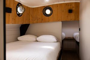 a bed in a room with wooden walls and two windows at Unieke beleving op het water, de Prinsenboot. in Spaarndam