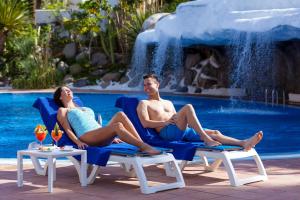 um homem e uma mulher sentados em cadeiras em frente a uma piscina em Hotel Best Tenerife em Playa de las Americas