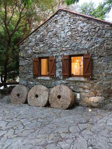 a stone building with two windows and two large boulders in front at Moinho das fragas in Figueiró dos Vinhos