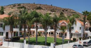 a building with palm trees in front of a mountain at Kotzias Beach Apartments in Pissouri