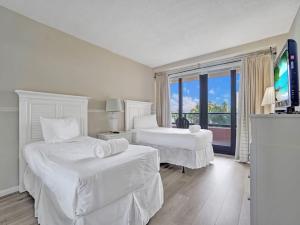 a white hotel room with two beds and a flat screen tv at Beachfront Ocean View Condo Beach Service 520 in Miami Beach