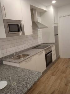 a white kitchen with a sink and a microwave at La casa del Timón.Planta baja in Muros