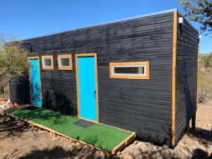 ein schwarzes winziges Haus mit blauen Türen und Gras in der Unterkunft Hostal El Boldal in La Estrella