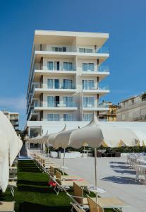 a large white building with tables and umbrellas at Hotel Galassia Suites & Spa in Lido di Jesolo