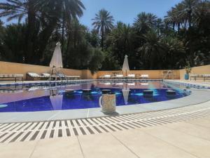 a large swimming pool with blue water and palm trees at Auberge Camping Atlas in Tinerhir