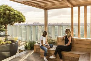 two women sitting on a wooden bench on a balcony at Manhattan Loft Gardens, Stratford in London