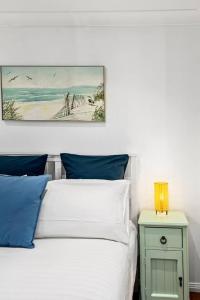 a bed with blue pillows and a picture on the wall at Rothery Escape - A Cosy Coastal Cottage in Bellambi