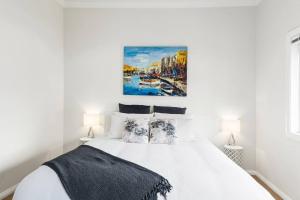 a bedroom with a white bed with a painting on the wall at Saltwater Escape - Live the Sand and Surf Lifestyle in Thirroul