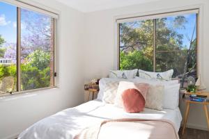 Schlafzimmer mit einem Bett mit weißer Bettwäsche und Fenstern in der Unterkunft 'Garden Escape' Serene Coastal Living in Wollongong 