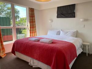 a bedroom with a bed with a red blanket and a window at HPG Villa formerly known as Pipi Hotel in Havelock North