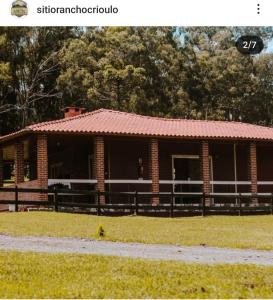 a brick house with a red roof on a field at Casa de Sítio Rancho crioulo in Urubici