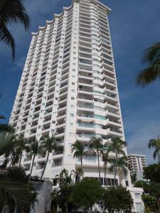 a tall white building with palm trees in front of it at Departamento en Acapulco La Palapa in Acapulco