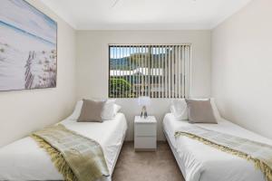 two beds in a white room with a window at Esplanade Escape - Beachfront Family Bliss in Thirroul