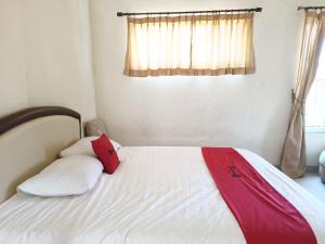 Un dormitorio con una cama blanca con almohadas rojas y blancas en RedDoorz Syariah near Rumah Sakit Umum Wisata UIT, en Balangberu