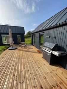 une terrasse en bois avec un grill et une maison dans l'établissement Pļavas vidū - romantiska brīvdienu māja, à Matīši