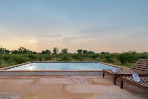 una gran piscina con 2 sillas en StayVista's Gaudhuli Farmstay - Outdoor Pool & Terrace with View, 