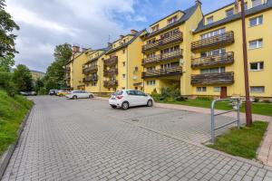 un aparcamiento con coches estacionados frente a un edificio amarillo en Apart-Invest Apartament Paryski en Szklarska Poręba