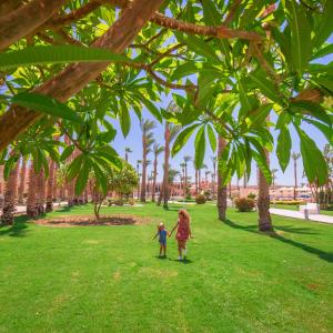 dos niños caminando en un parque bajo palmeras en Beach Albatros Aqua Park - Hurghada, en Hurghada