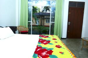 a bedroom with a bed with a floral comforter and a window at Sandy Palms Guesthouse in Hikkaduwa