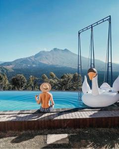 a man in a straw hat sitting in a pool with swans at Sari Sky Bali in Kubupenlokan