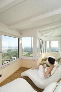 a woman laying on a bed in a room with windows at Al Mirador Resort in Selva di Fasano