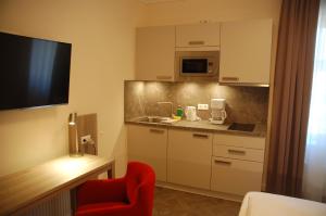 a room with a kitchen with a red chair and a tv at Aparthotel Weißenhorn in Weißenhorn