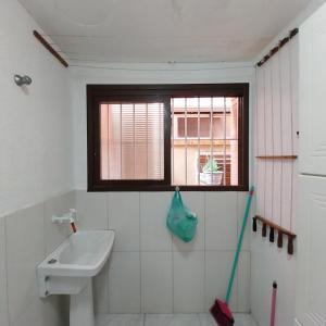 a bathroom with a sink and a window and a mop at Muito aconchegante perto do centro e da praia in Capão da Canoa