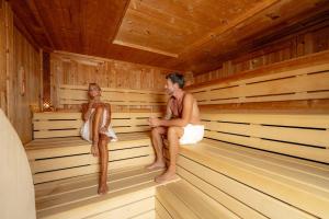 a man and woman sitting in a sauna at Monte Pana Dolomites Hotel in Santa Cristina in Val Gardena