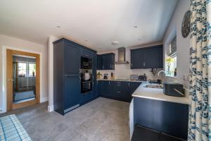 uma grande cozinha com armários azuis e um lavatório em Fleming Cottage - Contemporary Cotswold Home 