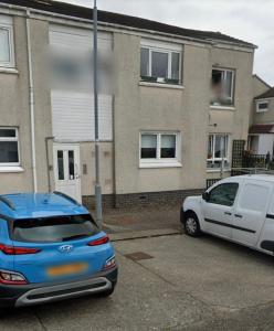 dos autos estacionados en un estacionamiento frente a un edificio en Holiday Apartment, Balloch, Loch Lomond en Balloch