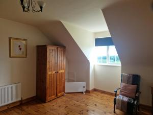 an attic room with a wooden cabinet and a chair at Forest View Dunmore Galway H54P897 in Dunmore