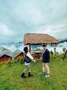 two people standing in the grass near a hut at Homestay Chân Mây Chiêu Lầu Thi in Hoàng Su Phì