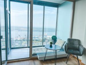 a room with a chair and a table and large windows at UP 34 FLOOR APARTMENTS in Klaipėda